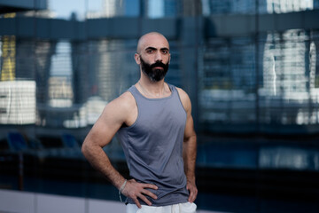 Fototapeta na wymiar With his hands on his waist, a middle aged man with muscular, toned arms and a graying beard poses in athletic wear. His strong, dark, handsome Middle Eastern features add visual interest.