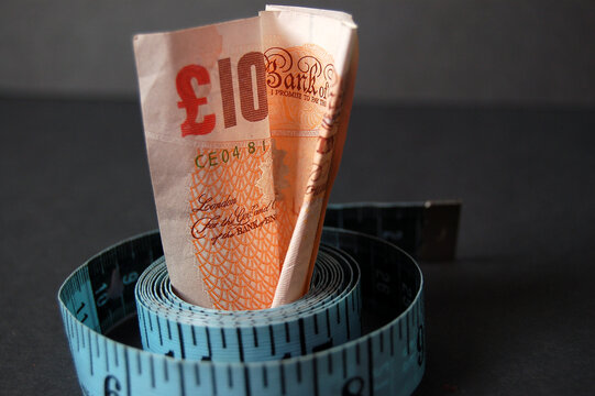 This is an image of a ten pound note and measuring tape, with a stack of pennies in the background.