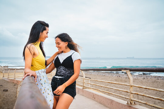 Young lesbian couple smiling while having a date outdoors at the beach promenade.