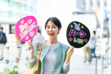 応援うちわを持ってライブ会場の前に立つ女性　推し活