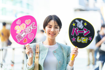 応援うちわを持ってライブ会場の前に立つ女性　推し活