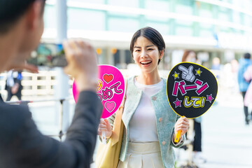 応援うちわを持ってコンサート会場の前に立つ女性　推し活