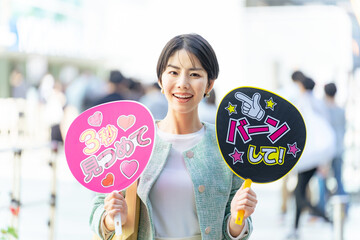 応援うちわを持ってライブ会場の前に立つ女性　推し活