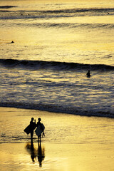 Fototapeta na wymiar Two surfers standing on the shore at sunset