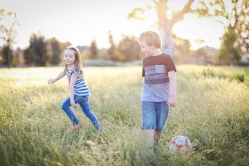 Boy and girl running through long grass playing soccer at the park. Aussie kids having fun outdoors in nature