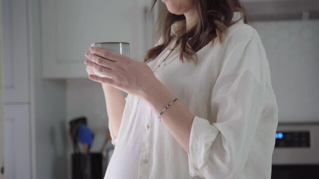 Pregnant woman drinking coffee. Caucasian girl enjoys her morning cup of coffee on her kitchen. Pregnancy and caffeine.