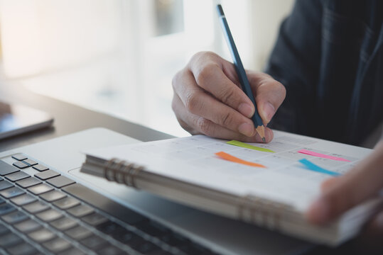 Event planner timetable agenda plan on year 2023 schedule event. Business man checking timetable, taking note on calendar planner notebook on office table. Calendar event plan, work planning