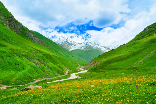 Green pasture and Patara enguri river against highest georgian mountain Shkhara near Ushguli in Georgia.