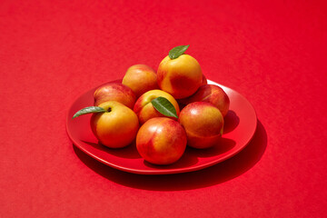 A dish in round-shaped containing several peaches, put on red background. Peach (Prunus persica) may help improve and protect your skin