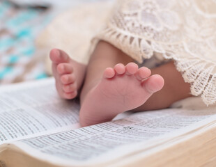 Close up shot of the soft tender legs of a Nigerian new born baby child placed on an open Bible book