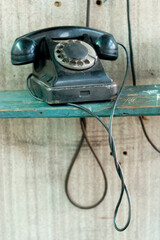 old scratched phone with dialing disk on the wooden scratched table. Background wall is smoothed