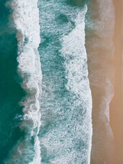 Fototapeta na wymiar Simple top down drone view of waves coming ashore a sandy beach in symmetrical lines from left to right. Good for background or wallpaper. 