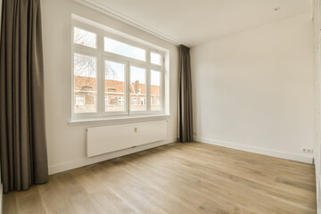 an empty room with wood flooring and large window overlooking the street in front of the house, on a sunny day