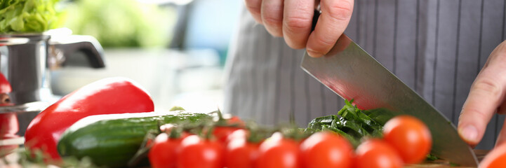 Cook cuts tomatoes and cucumbers on cutting board. Cooking vegetable salad concept