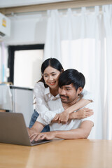 Young married couple showing happy smiling faces and using computers and notebooks to calculate household income and expenses while relaxing at home.