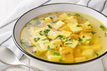 Zuppa imperiale is a simple but delicious soup made from a rich chicken broth finished with cubes of baked semolina and Parmesan closeup on the plate on the table. Horizontal