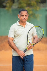 vertical shot of Happy smiling senior men with racquet and ball looking camera at tennis court - concept of confident, successful and relaxation