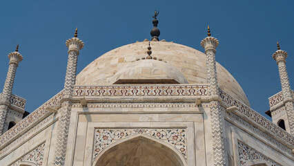 The upper part of the Taj Mahal mausoleum against the blue sky. White marble dome with spires....