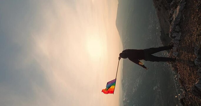 Vertical Video Rainbow LGBT Flag on Sunset Sky in the Mountains. Male Man Waving lgbtq gay pride flag-lesbian, gay, bisexual, transgender social movements. Concept of freedom love same-sex couple, 4 K