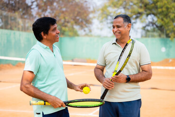 Happy indian senior tennis playing friends laughing while talking at tennis court - concept of...