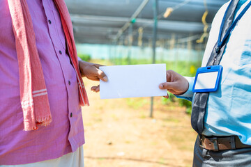Close up shot of indain farmer receiving notice from banking employee at greenhouse for loan...