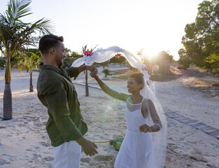 Caucasian newlywed couple holding hands and dancing at wedding ceremony at beach during sunset