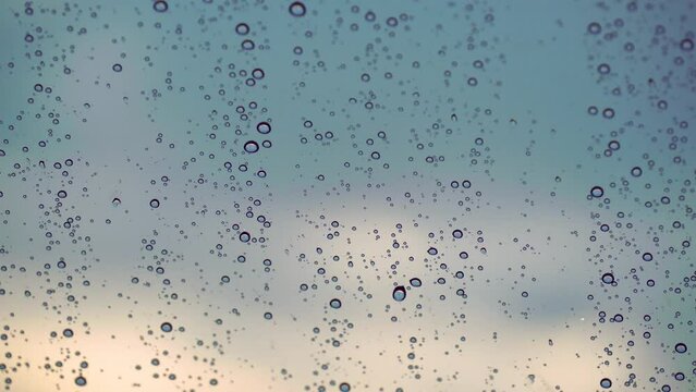 Water drops descend on the glass window in rainy weather against the blue sky.