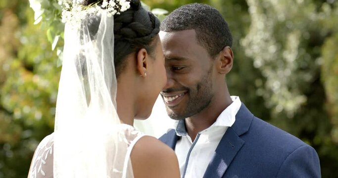 African american couple smiling and touching heads at their wedding in sunny garden, slow motion