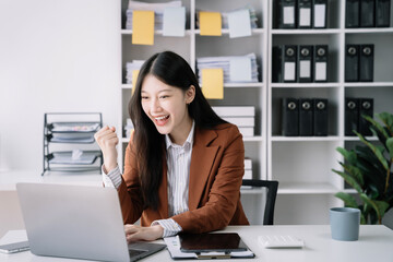 Smiling young asian woman succeeding in business using laptop and computer while doing some...