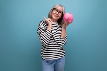 pleasant middle-aged woman 50 years old holding a piggy bank with savings on a bright background...