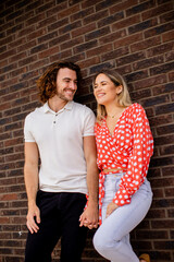 Smiling young couple in love standing in front of house brick wall