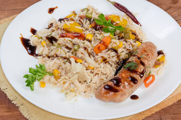 Serving of rice with vegetables, baked sausage seasoned with sauce