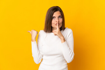 Young Slovak woman isolated on yellow background pointing to the side and doing silence gesture