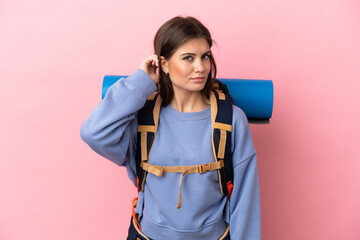 Young mountaineer woman with a big backpack isolated on pink background having doubts