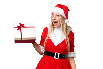 Young blonde woman with christmas hat and holding a gift over isolated chroma key background with surprise and shocked facial expression