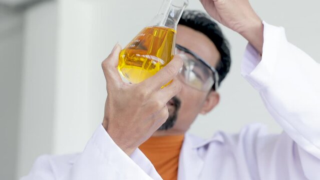 Asian male scientist analyzing Liquid Biochemicals in Laboratory Flask. Advanced Scientific Biotechnology Laboratory,  processing of laboratory sample in a flask, titration with reagent from a burette