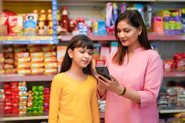 Mother and daughter in grocery store using smartphone.