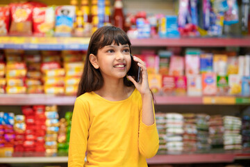 Indian girl talking on smartphone at grocery shop.