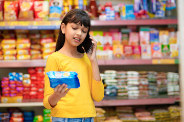 Indian girl talking on smartphone at grocery shop.