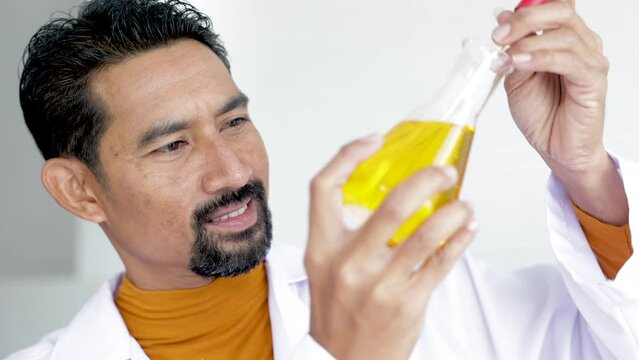 Asian male scientist analyzing Liquid Biochemicals in Laboratory Flask. Advanced Scientific Biotechnology Laboratory,  processing of laboratory sample in a flask, titration with reagent from a burette