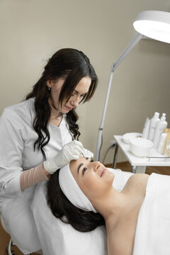 The photo reflects the therapeutic procedure of deep cleansing of the skin of the face, during which a beautiful woman finds harmony and relaxes in a beauty clinic. Cosmetologist works in the office