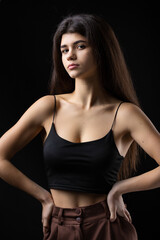 Fototapeta na wymiar Classic studio portrait of a young brunette dressed in a black top, who is sitting on a chair against a black background.
