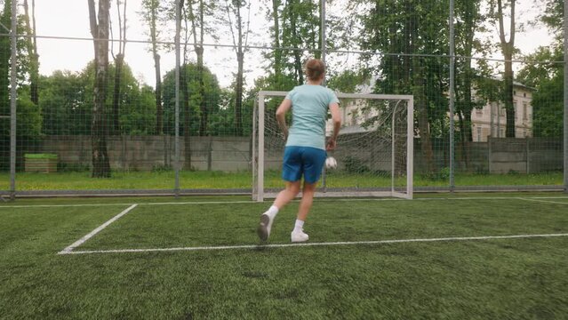 A female football player is training on a mini-football stadium. The footballer is dribbling the ball forward while practicing fancy footwork and shot on goal, scoring a goal. Back full shot.