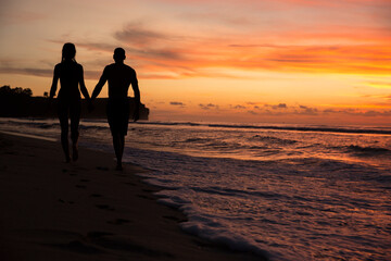silhouette of couple walking on the beach at sunset