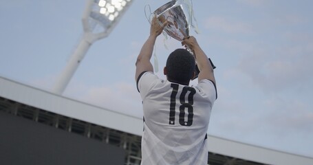 Portrait of African Black male soccer football player celebrating victory in the championship, lifting the trophy above his head in a huge stadium