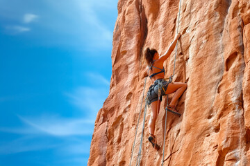 Side view of a young slender woman rock climbing on a rock. A woman climbs a vertical rock wall against a blue sky. Generative AI