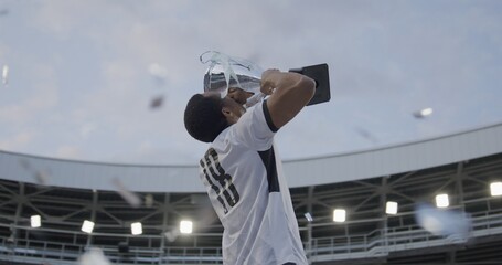 Portrait of African Black male soccer football player celebrating victory in the championship, lifting the trophy above his head in a huge stadium