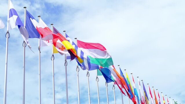 national flags of Europe and other countries on satin flutter in wind in blue sky near building of European Parliament, state symbols, concept of international cooperation, global business
