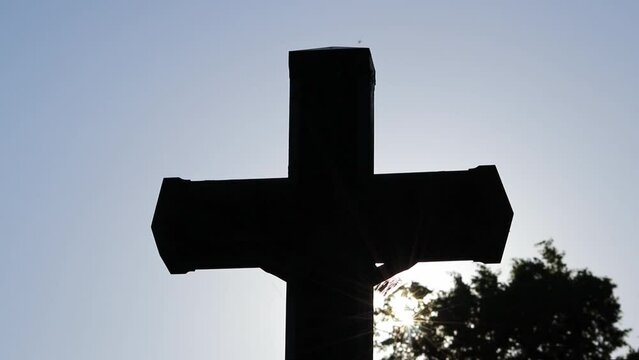 Holy cross glowing in evening sunset sunshine as symbol for jesus christ on cross in silhouette as christianity and spritual crucification or resurrection after death of jesus christ on cemetery grave