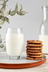 A glass of milk and cookies on a plate on a light background